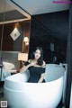 A woman in a black dress sitting in a bathtub.