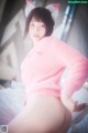 A woman in a pink sweater is posing on a bed.