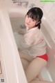 A woman in a white shirt and red panties sitting in a bathtub.