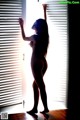 A nude woman standing in front of a window.