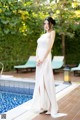 A woman in a white dress standing next to a pool.