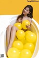 A woman sitting in a bathtub filled with yellow balloons.