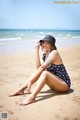 A woman sitting on the beach in a bathing suit and hat.