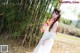 A woman in a white dress standing in front of a bamboo forest.