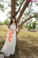 A woman in a white dress standing next to a tree.