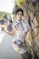 A woman in a floral dress holding a fan.