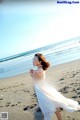 A woman in a white dress walking on a beach.