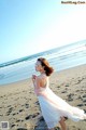 A woman in a white dress walking on the beach.