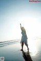 A woman in a white dress standing on the beach.