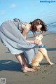 A woman kneeling down petting a dog on the beach.