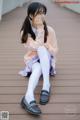 A young girl sitting on a wooden floor with her hand on her chin.