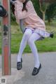 A woman in a pink sweater and white tights leaning against a pole.