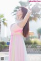 A woman in a pink and yellow dress standing on a beach.