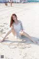 A woman sitting on the beach in a white dress.