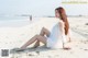 A woman in a white dress sitting on the beach.