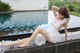 A woman in a white dress sitting by a pool.