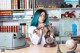 A woman with blue hair sitting at a desk holding a telephone.