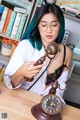 A woman with blue hair sitting at a desk with a clock.