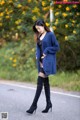 A woman in a blue cardigan and thigh high boots standing on a road.