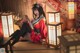 A woman in a red kimono sitting on the floor next to lanterns.