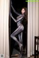 A woman in a silver bodysuit leaning against a door.