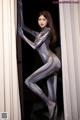 A woman in a silver bodysuit leaning against a wall.