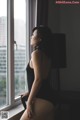 A woman in a black bodysuit sitting by a window.