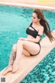 A woman in a black bathing suit sitting on the edge of a swimming pool.