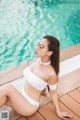 A woman in a white bikini sitting by a swimming pool.