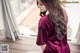 A woman in a maroon robe sitting on a window sill.