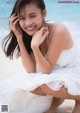 A woman in a white dress sitting on the beach.