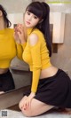 A woman in a yellow top and black skirt posing in front of a mirror.