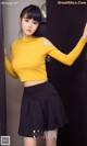 A woman in a yellow top and black skirt posing for a picture.