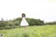 A woman in a white dress and straw hat standing in a field.