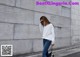 A woman wearing a white sweatshirt and jeans standing in front of a wall.