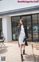 A woman in a white dress and black coat is walking outside of a building.