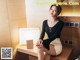 A woman sitting on top of a wooden desk next to a lamp.