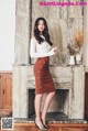 A woman standing in front of a fireplace wearing a brown skirt.