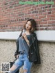 A woman leaning against a brick wall holding a drink.