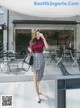 A woman in a red top and plaid skirt is walking down the street.