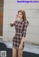 A woman in a plaid dress is posing for a picture.