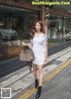 A woman in a white shirt dress is walking down the street.