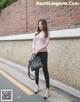 A woman standing in front of a brick wall holding a black bag.