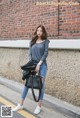 A woman standing in front of a brick wall holding a black bag.