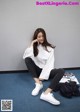 A woman sitting on the floor wearing white sneakers.