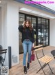 A woman standing in front of a building wearing a black sweater and jeans.