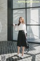 a woman standing in front of a window wearing a white shirt and black skirt