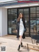 a woman in a white dress and black coat walking down a wooden floor