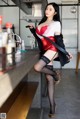 A woman in a red dress and black stockings posing at a bar.