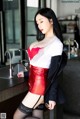 A woman in a red and white top and black skirt posing in a kitchen.